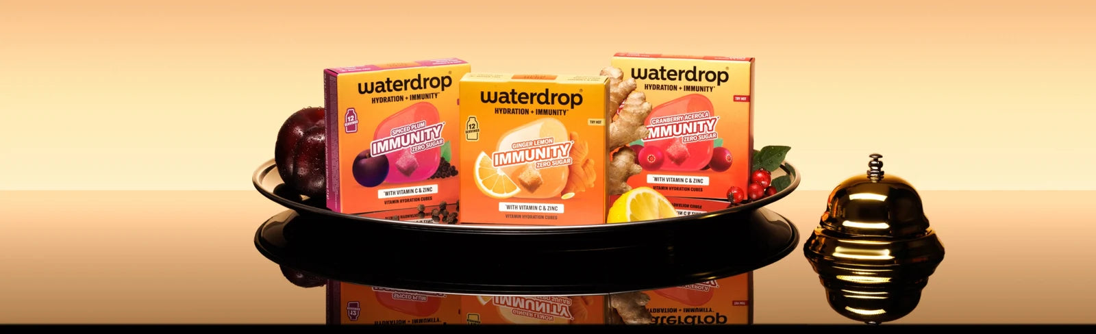 Plateau avec trois boîtes Waterdrop sur une surface réfléchissante et une petite bouteille décorative à droite.